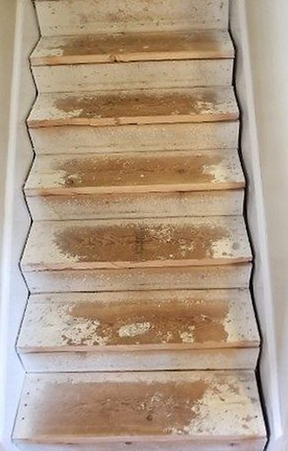 A staircase stripped back to bare treads, patchy with old adhesive and stain residue